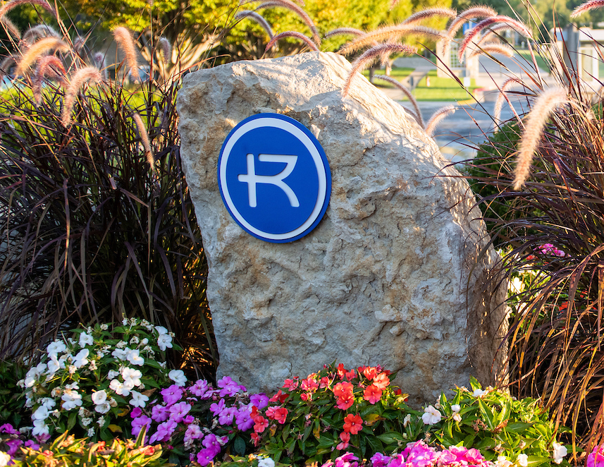Rockhurst logo on large limestone rock in flower garden