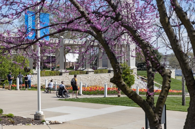 Spring on campus as a student walks next to another in a wheelchair