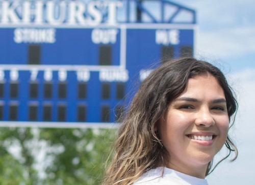 BreAnna Droge headshot with softball scoreboard in the background