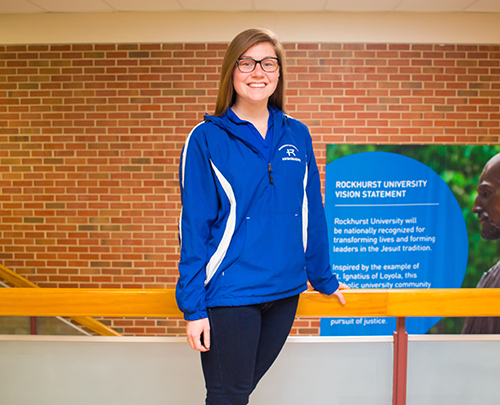 Sydney Hunter stands in front of a stairwell in Massman hall. 