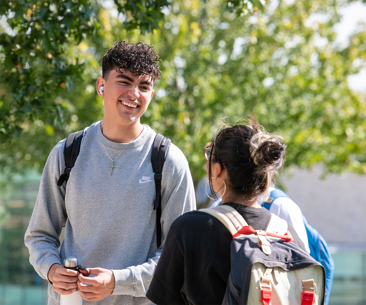 Male student smiles with a friend on the Quad