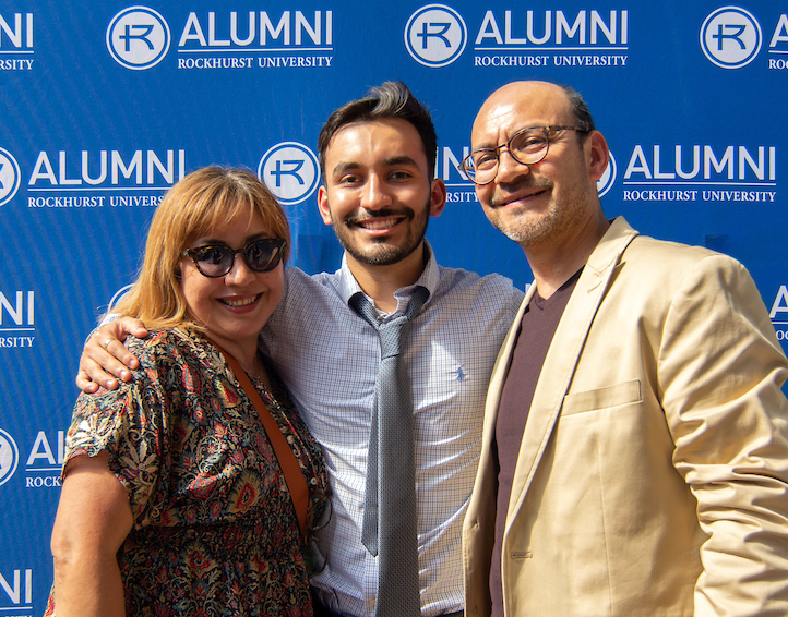 Parents with grad in front of Alumni backdrop