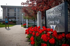 Helzberg School of Management sign with tulips as student walks by