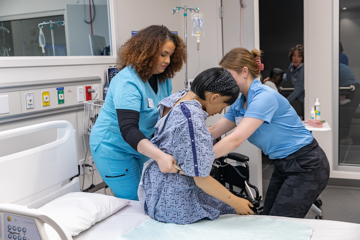 An OT and PT student work to move a mannequin from a bed to a chair