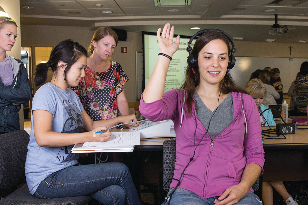 A student raises her hand while undergoing an audiology hearing test