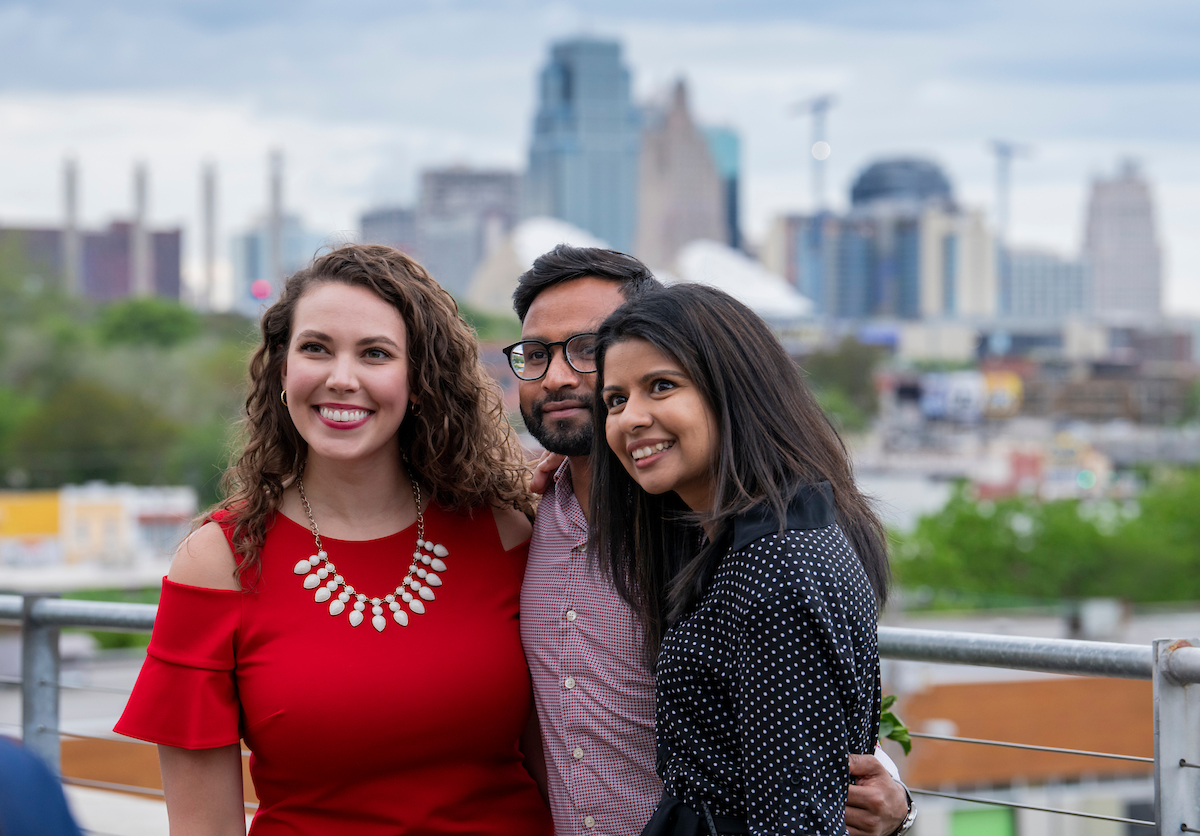 3 grad students pose in front of Kansas City skyline