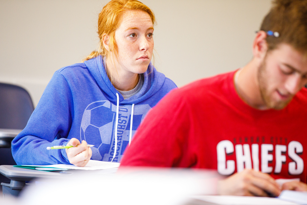 A student holds a pen as she looks up from her paper while in class