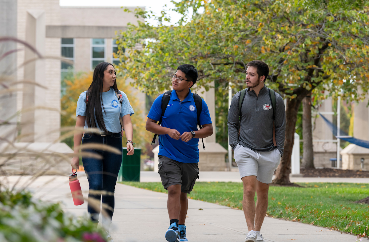 Three students, talking to each other, walk on campus together.