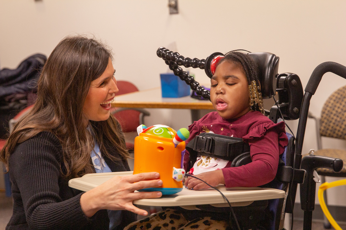 An occupational therapist works with a child in a wheelchair, showing her an electric toy