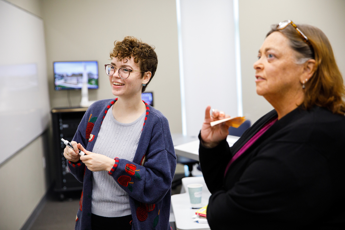 A teacher and student look at a white markerboard in a classroom