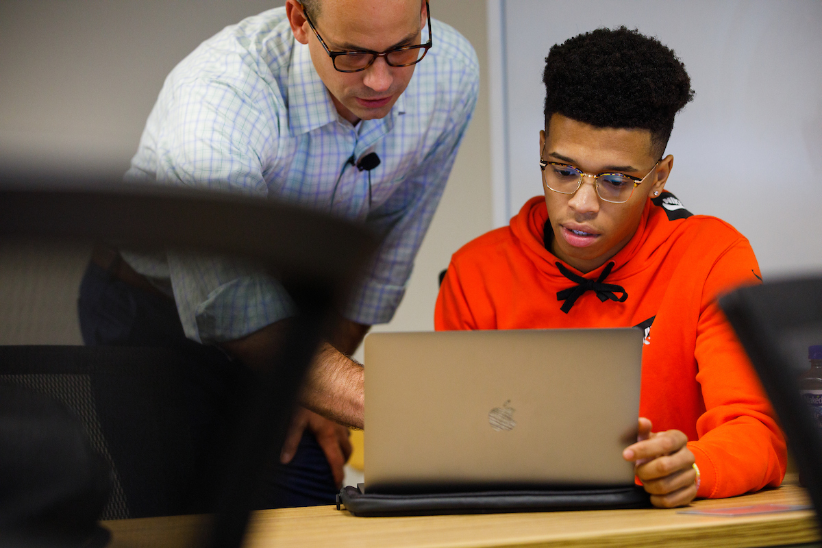 A professor helps a student, both looking at a laptop