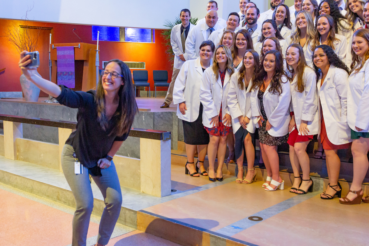 A PT professor takes a selfie with a group of graduates posed behind her