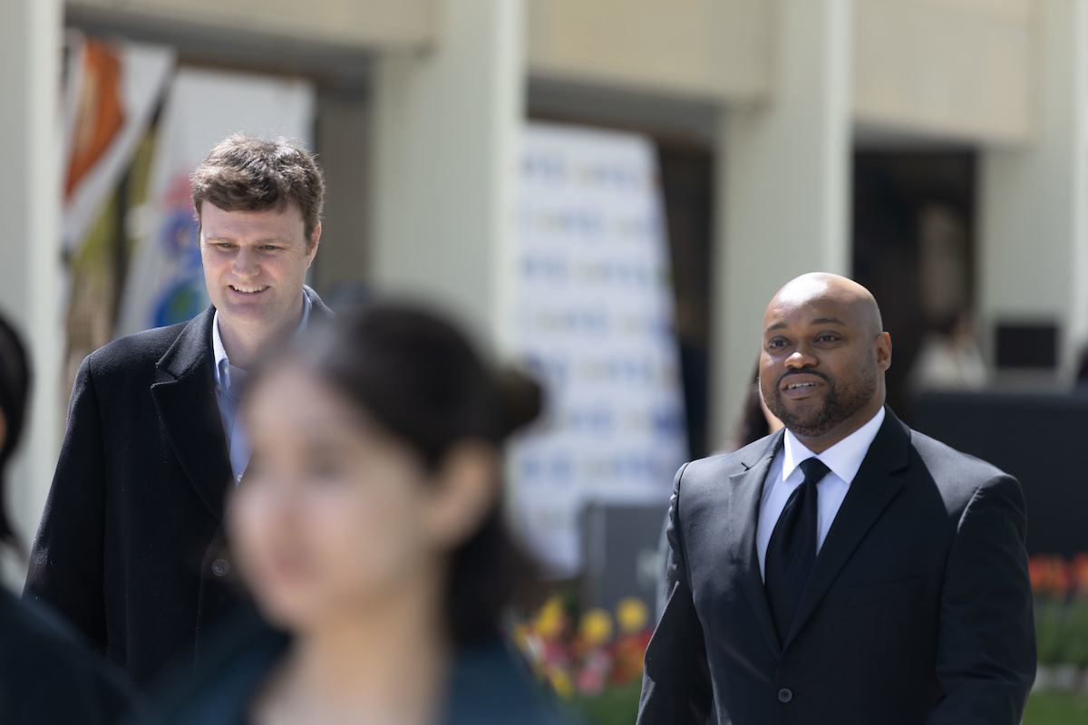 Two students in suits walk toward the camera as a woman in the foreground does the same