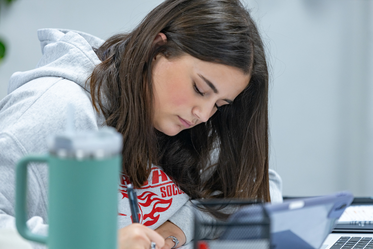 A student studies at the Learning Center, writing with a pencil while leaning over her notebook