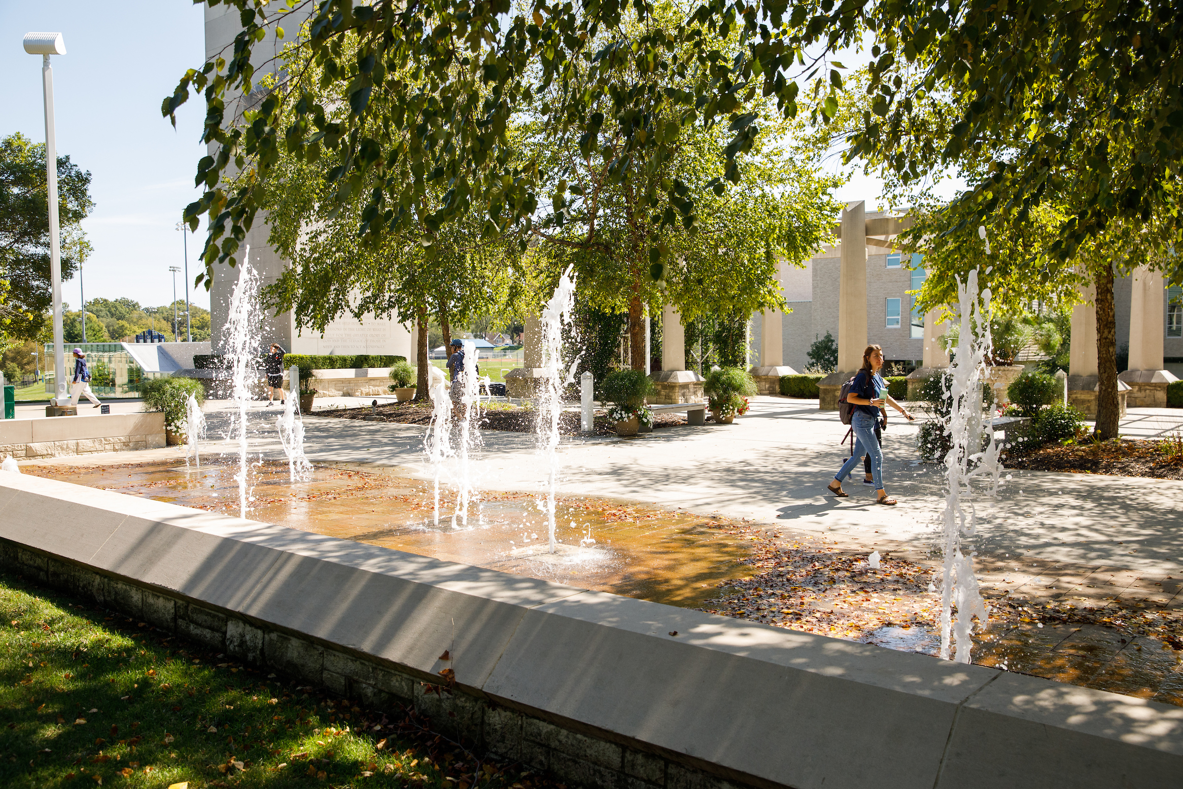 Fountains and trees in the foreground as students walk by.