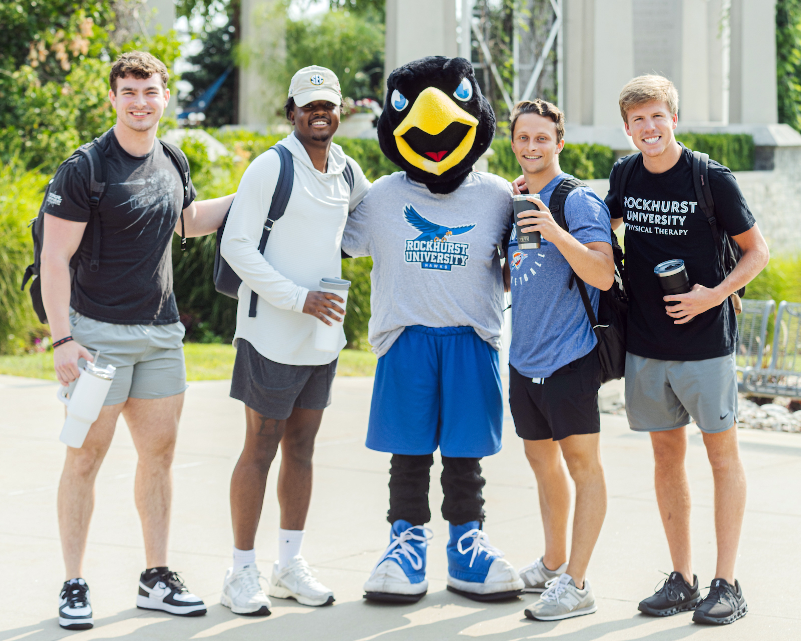 Rockhurst University mascot Rock E. Hawk with four male students holding cups. 