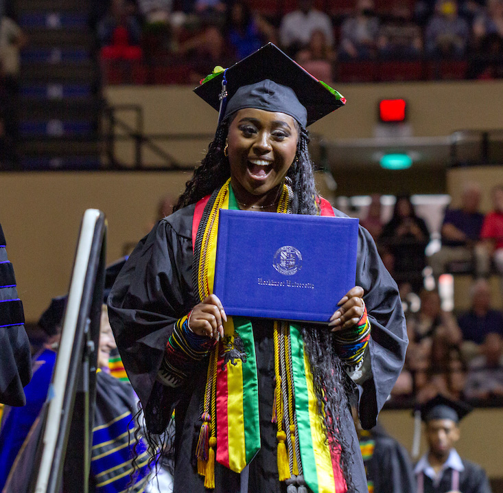 A new graduate looks at the camera and celebrates on stage