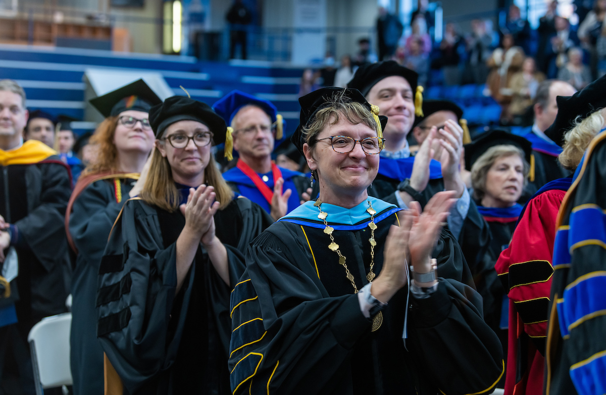 Faculty applaud while dressed in commencement regalia