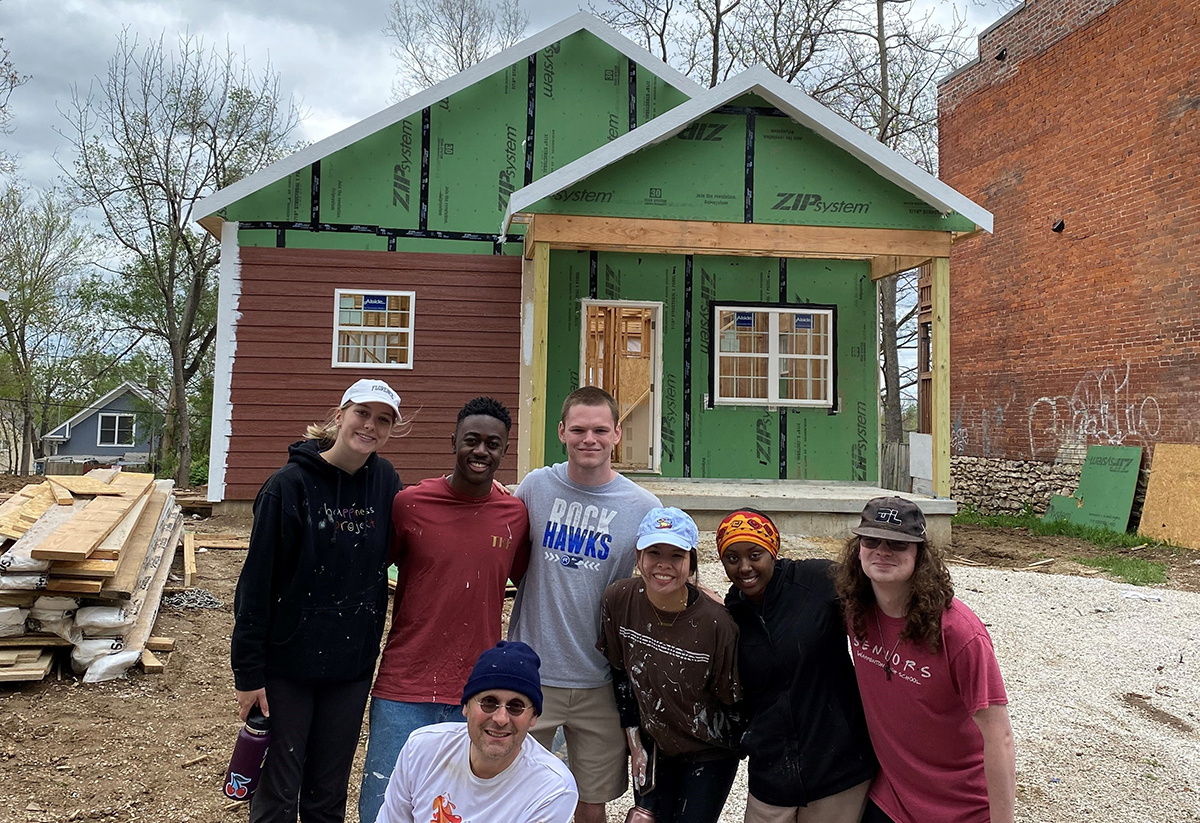 A group of students poses in front of a Habitat for Humanity house. 