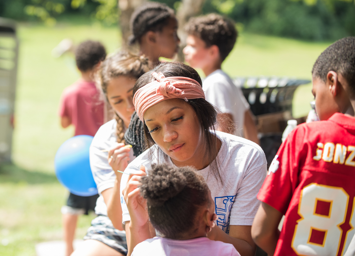 Student volunteers paint kids' faces as part of a community outreach project