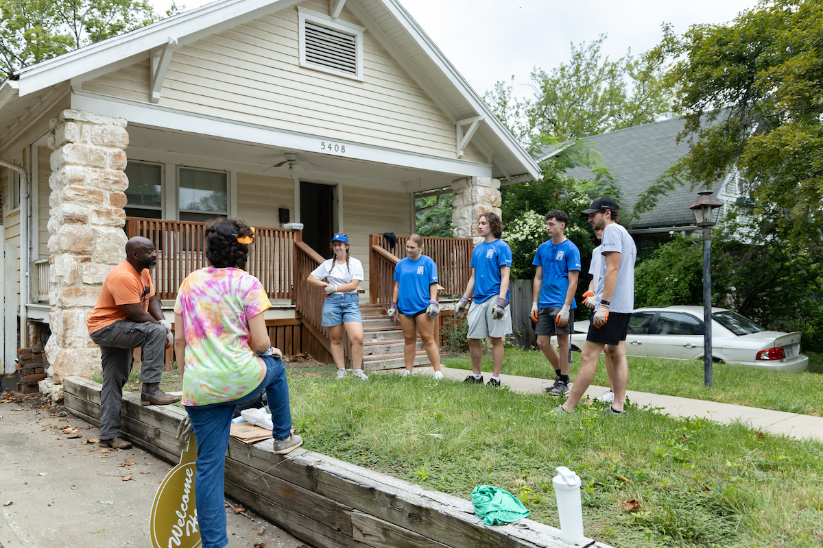 Student workers talk with a local couple in front of a house