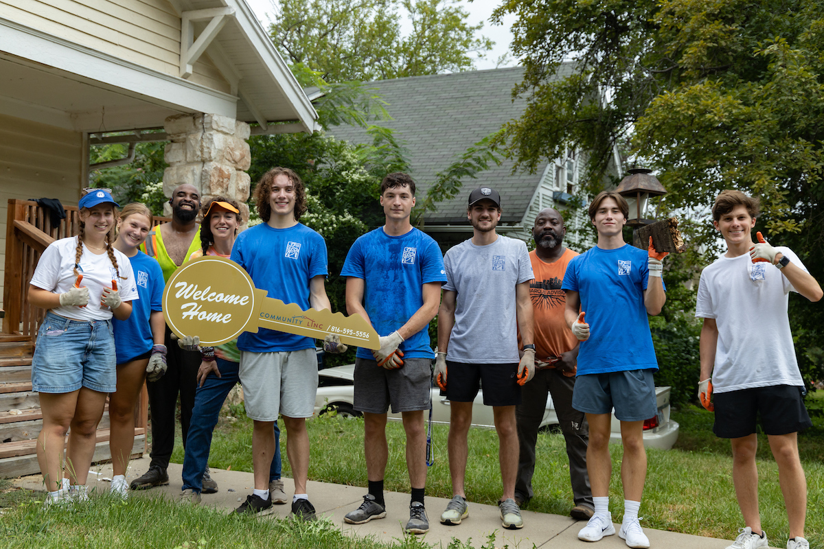 Student volunteers pose in front of a house with an oversized house key that says Welcome Home