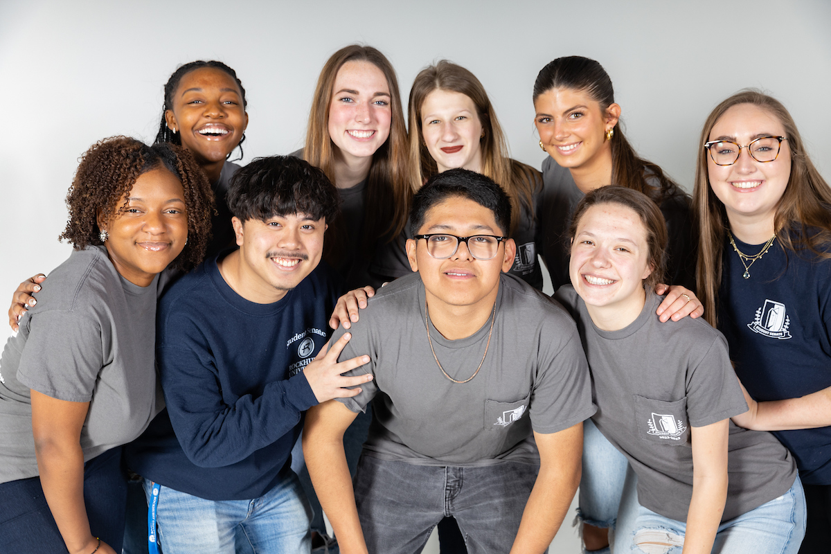 Group of diverse students smiling with arms around each other, each a representative from a different student organization