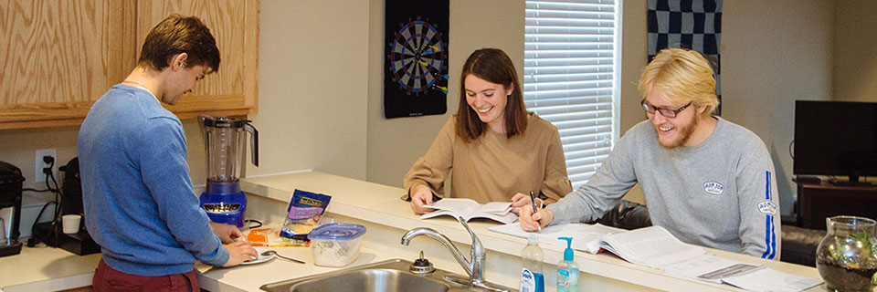 Students sit at the kitchen bar while another prepares food on the counter 