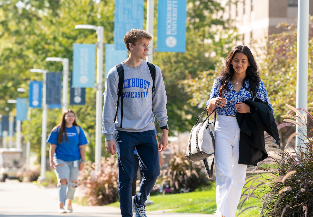 Three students walk down the main sidewalk on campus