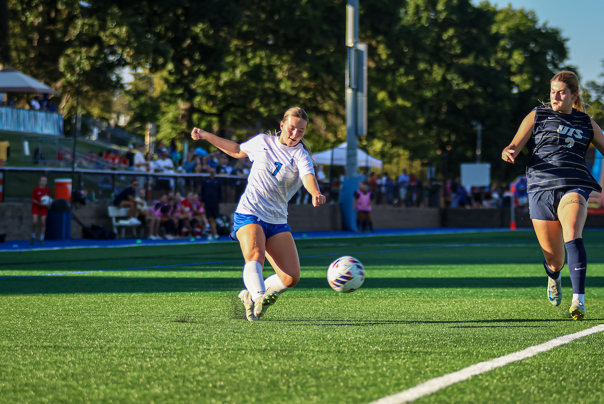 A women's soccer player strikes a ball in front of a crowd of supporters