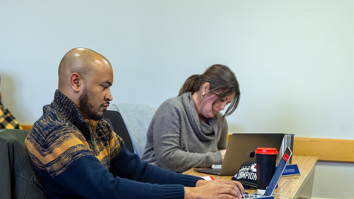 Two emba students type on laptops during class