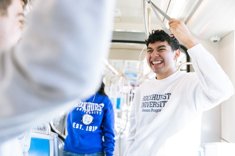 A student wearing a white Rockhurst University crewneck holds onto a handle while on the Kansas City streetcar