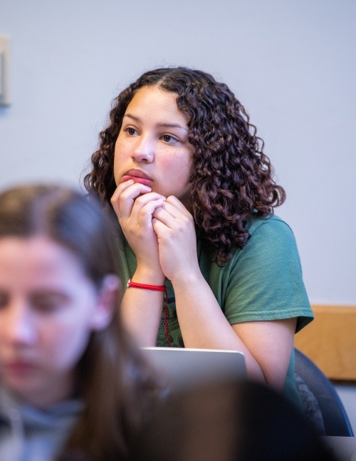 A female student rests her head on her hands as she listens in class