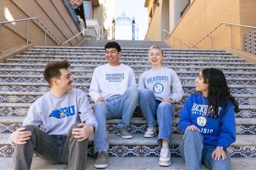 Four Rockhurst University students in RU shirts sit on decorative stairs