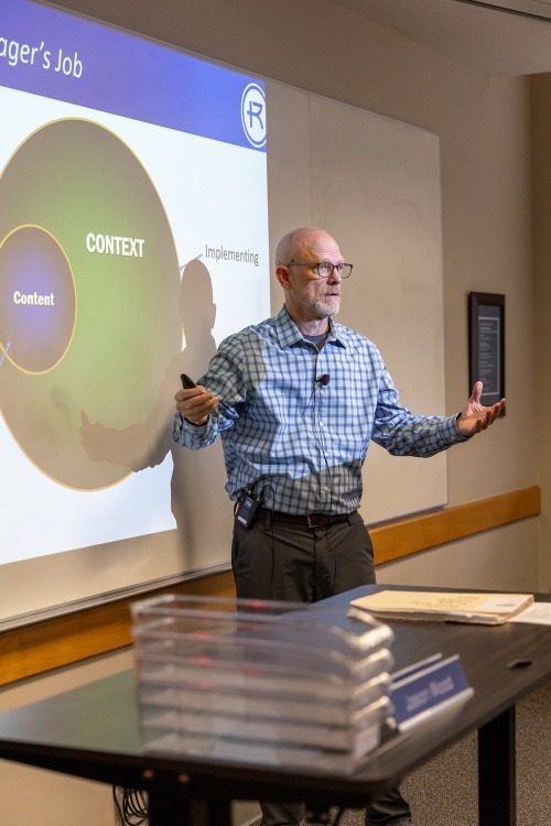 An EMBA professor stands in front of a slide talking about content and context