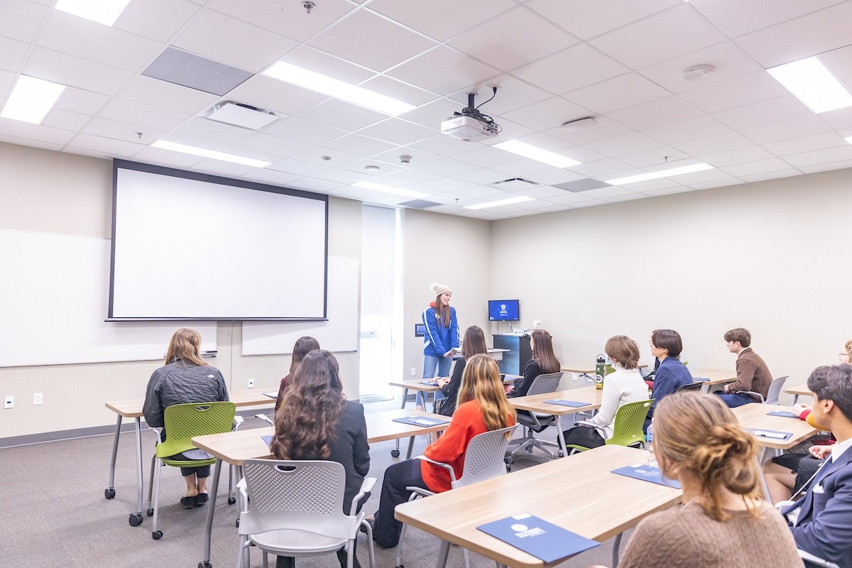 A classroom full of science data students are watching another student present at the front of the classroom.