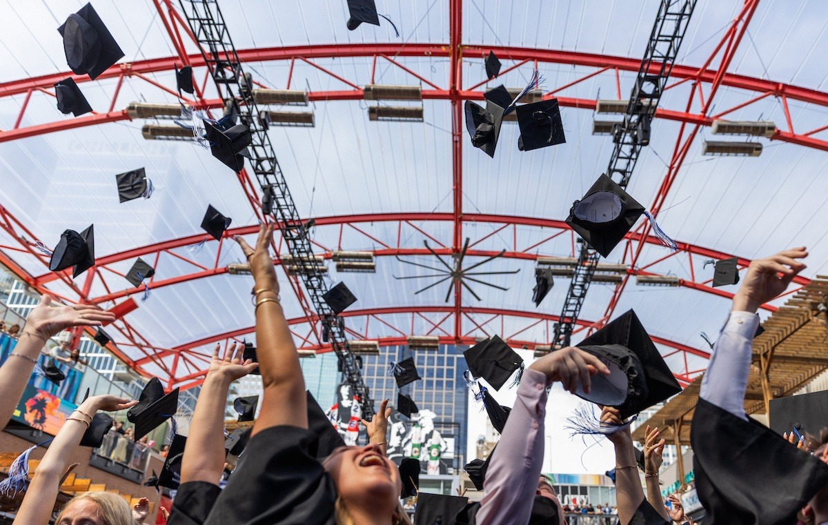 Graduates throw their caps in the air at KC Live during the 2026 Commencement