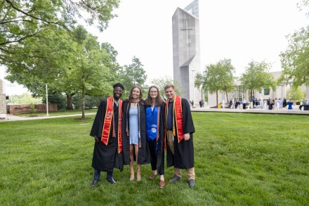 Four grads in cap and gowns in front of the bell tower