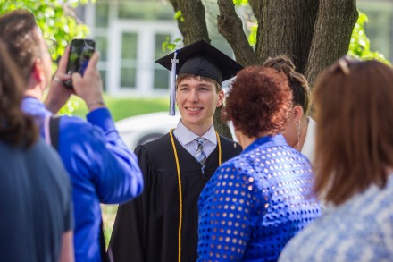 A male graduate poses as a family member takes a photo with their phone
