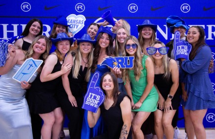 A group of female athletes pose for a group photo with Hawks props