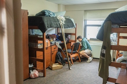 A male student shorts through belongings in his dorm room