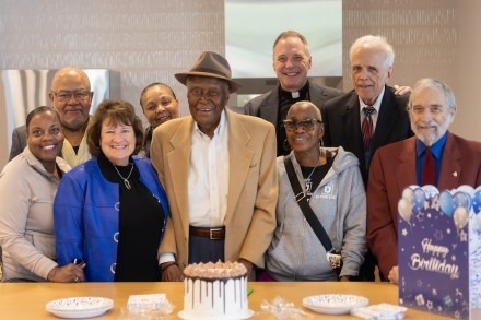 Alvin Brooks stands behind a birthday cake surrounded by family and RU leaders
