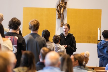 A female student stands at the front of the chapel beneath a crucifix during an Ash Wednesday Mass
